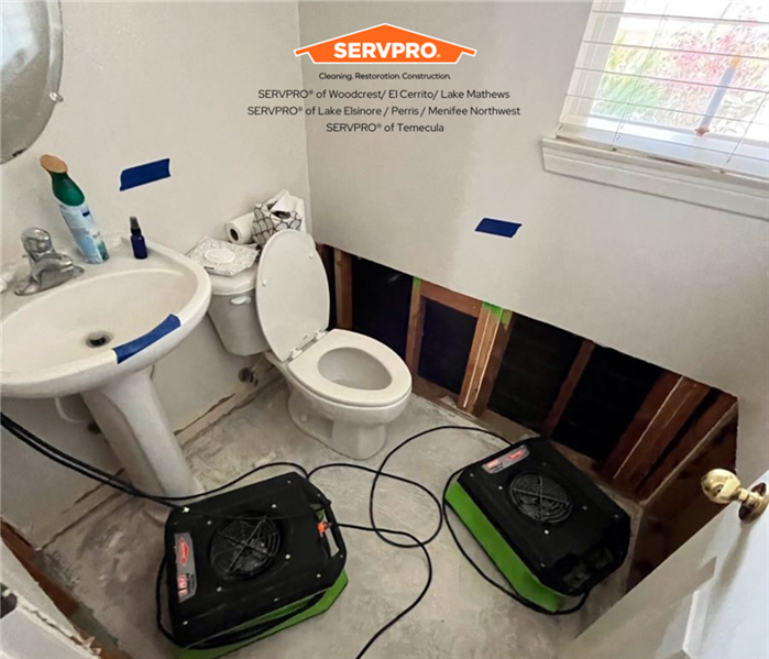 a water damaged bathroom with the walls and hardwood flooring taken out and air movers placed on floor